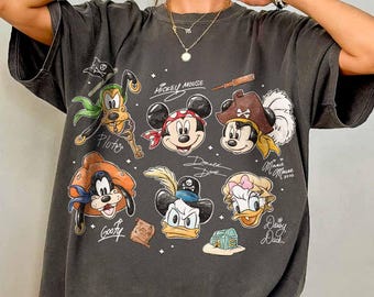 May include: Dark gray t-shirt featuring cartoon pirate characters including Mickey Mouse, Minnie Mouse, Donald Duck, and Goofy. The shirt has a vintage, distressed look with the characters' names and other pirate-themed elements.
