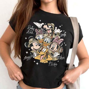 Pu&ograve; includere: T-shirt nera con una grafica dei personaggi Disney Topolino, Minnie, Paperino, Paperina, Pippo e Pluto in tenute da safari. I nomi dei personaggi sono scritti sulla maglietta.
