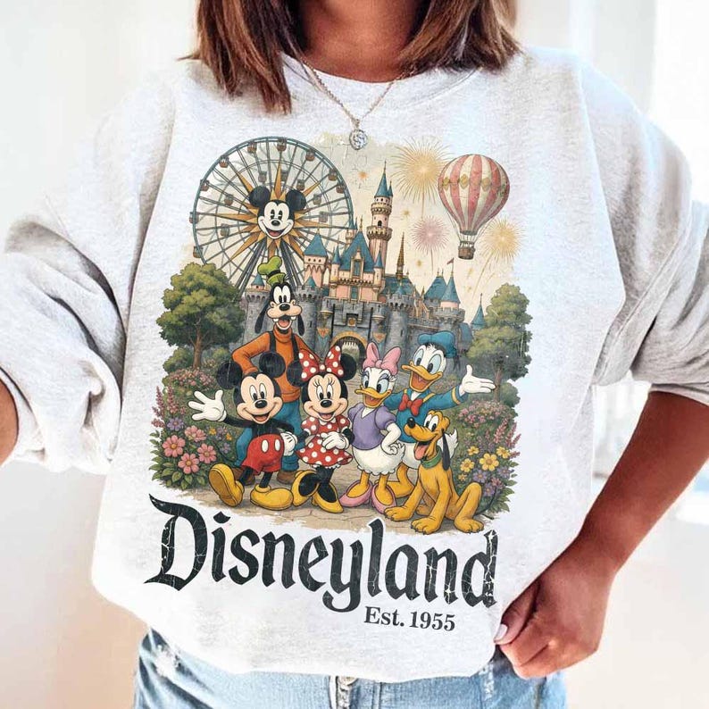 May include: A light grey crewneck sweatshirt featuring a colourful graphic of Mickey Mouse, Minnie Mouse, Goofy, Donald Duck, Daisy Duck, and Pluto in front of a castle, a Ferris wheel, and a hot air balloon. The text reads Disneyland Est. 1955.