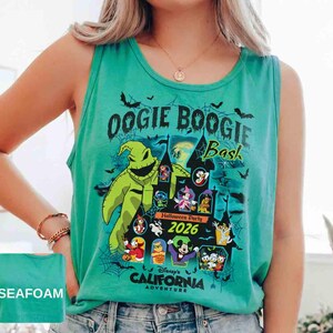 以下が含まれることがあります： 「Oogie Boogie Bash」の文字と、ウギー・ブギーや他のディズニーキャラクターのグラフィックが特徴の、シーフォームグリーンのタンクトップ。「Halloween Party 2026」と「Disney's California Adventure」の文字も含まれています。