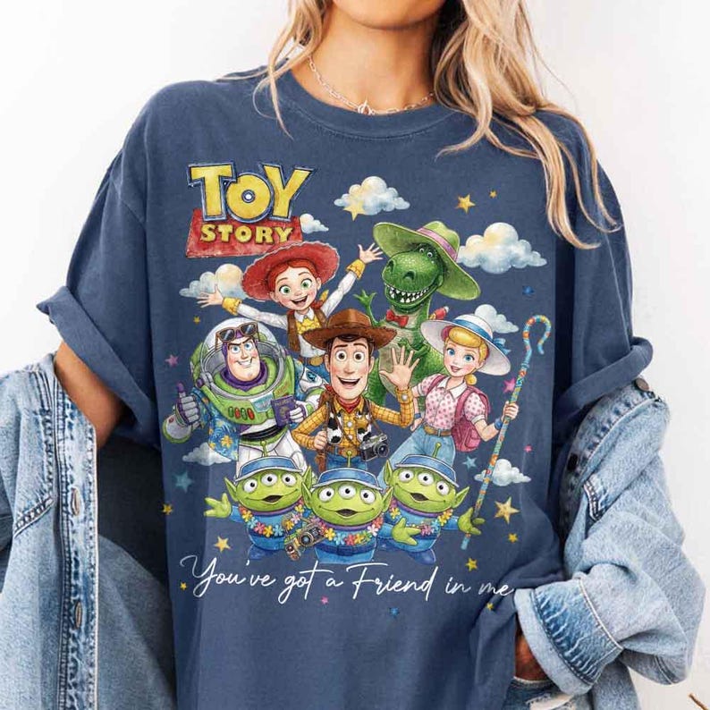 May include: Navy blue t-shirt featuring a colorful graphic of Toy Story characters, including Woody, Buzz Lightyear, and the aliens. The text "TOY STORY" is at the top, with "You've got a Friend in me" below. The shirt has a classic crew neck.