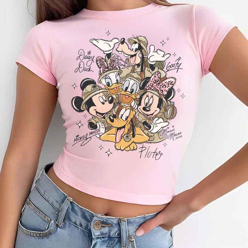 Pu&ograve; includere: Una maglietta rosa chiaro a maniche corte con una grafica dei personaggi Disney Topolino, Minnie, Paperino, Paperina, Pippo e Pluto. La grafica include i nomi dei personaggi e l'anno 2020.
