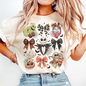 May include: Cream-coloured sweatshirt featuring colourful illustrations of characters and bows from The Nightmare Before Christmas. The design includes Jack Skellington, Sally, Oogie Boogie, and other iconic elements, ideal for fans of the movie.