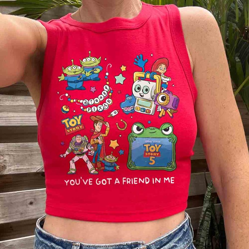 K&ouml;nnte beinhalten: Ein leuchtend rotes &auml;rmelloses bauchfreies Oberteil mit einem bunten Grafikdruck von Disney Pixar Toy Story Charakteren wie Woody, Buzz Lightyear und Aliens. Das Design enth&auml;lt den Text Toy Story, Toy Story 5 und You've Got A Friend In Me.