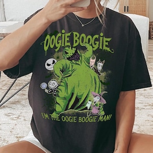 May include: Dark gray t-shirt featuring a green Oogie Boogie character from The Nightmare Before Christmas. The shirt has the text "Oogie Boogie" and "I'm the Oogie Boogie Man!" in green. Other characters are also featured.