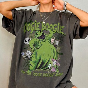 May include: Dark gray t-shirt featuring a green Oogie Boogie character design with the text "Oogie Boogie" and "I'm the Oogie Boogie Man!". The design includes other characters and spiderwebs. The shirt has short sleeves.