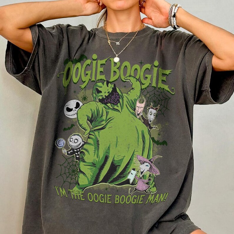 May include: Dark gray t-shirt featuring a green Oogie Boogie character design with the text "Oogie Boogie" and "I'm the Oogie Boogie Man!". The design includes other characters and spiderwebs. The shirt has short sleeves.