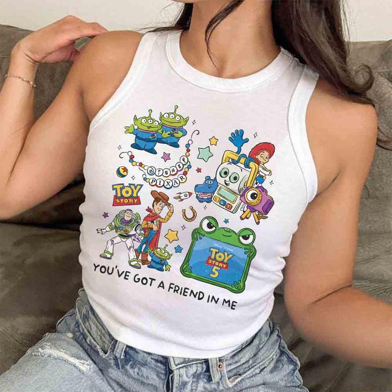 K&ouml;nnte beinhalten: Ein wei&szlig;es &auml;rmelloses Tanktop mit einem bunten Grafikdruck von Toy Story-Figuren, darunter Buzz Lightyear, Woody und verschiedene Aliens. Das Design enth&auml;lt den Text Disney Pixar, Toy Story, Toy Story 5 und You've Got A Friend In Me.