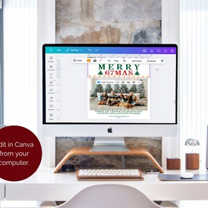 May include: A computer monitor displays a Christmas card design with the text "MERRY 67MAS" and a family photo. The card is being edited in Canva. The computer sits on a white desk with a wooden stand, keyboard, and speakers.