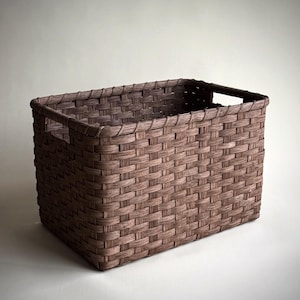 May include: A rectangular storage basket with a woven pattern in a dark brown wood-like finish. The basket features a sturdy rim and integrated cutout handles on the shorter sides, providing a structured and open design for holding various items.
