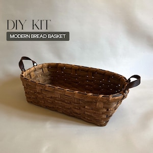 May include: A rectangular woven brown basket with two dark brown leather handles attached by silver-toned metal rivets. The text DIY KIT MODERN BREAD BASKET is printed in the upper left corner. The basket features a classic over-under weave pattern.