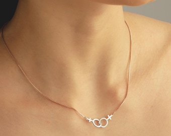 May include: A silver necklace with a delicate chain and a pendant featuring two interlocking circles with a small cross inside each circle.