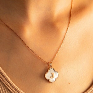 May include: A gold chain necklace with a white clover-shaped pendant featuring the letter "J" in gold.