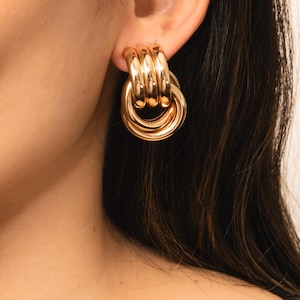 May include: Gold-toned knot-shaped earrings. The earrings are made of multiple interlocking circles.