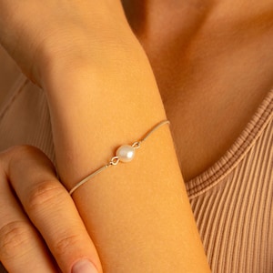 May include: A delicate silver chain bracelet with a single white pearl charm.