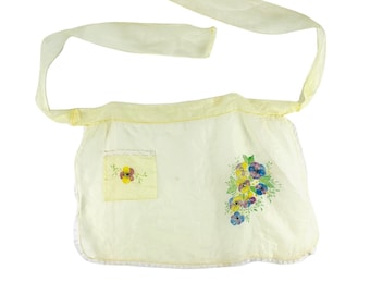 May include: A yellow apron with a floral design and a pocket. The apron has a tie at the neck and a tie at the waist.
