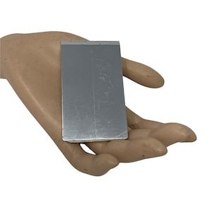 Puede incluir: Un espejo compacto plateado con un dibujo simple de una cara en la parte delantera.