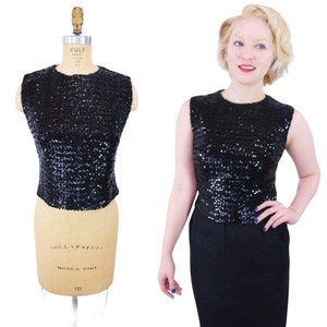 May include: A sleeveless black sequined top with a round neckline. The top is made of small, iridescent sequins.