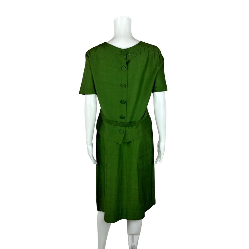 May include: A green dress with a short sleeve and a button down back. The dress has a belt and a skirt that falls to the knee.