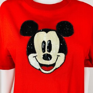 May include: Red short-sleeved t-shirt with a large sequined Mickey Mouse design.