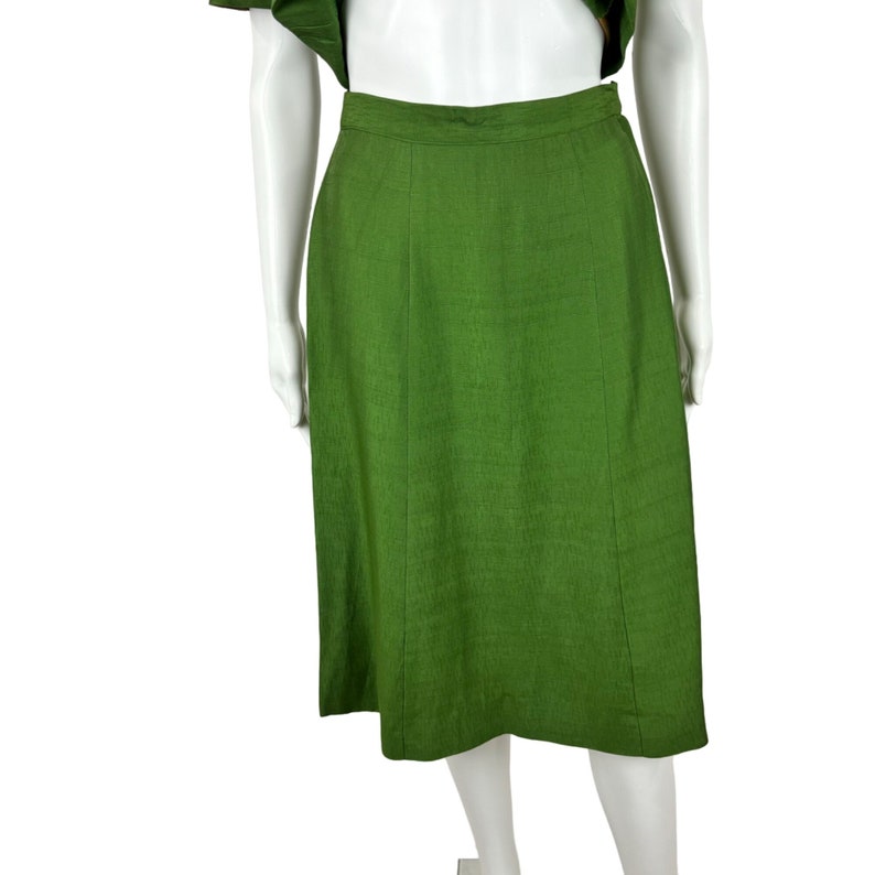 May include: A green midi skirt with a straight silhouette and a simple design. The skirt is made of a textured fabric and has a zipper closure in the back.