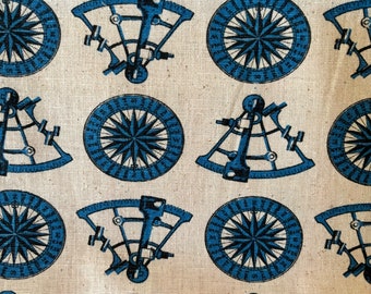 May include: A white fabric with a repeating pattern of blue compasses and sextants. The compasses have a black and white design with a blue outer ring. The sextants are blue and white with a black design.