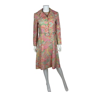 May include: A vintage floral print dress and jacket set. The set features a knee-length dress and a cropped jacket, both in a pastel color palette of pink, yellow, and green. The fabric is covered in a delicate floral pattern, creating a retro aesthetic.