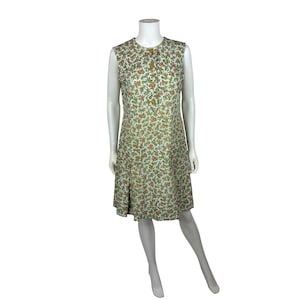 May include: A sleeveless white dress with a floral print in shades of green, orange, and yellow. The dress has a round neckline and a button closure at the front. The dress has a slightly flared skirt.