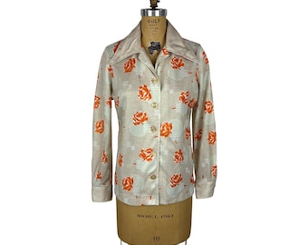 May include: Beige button-up shirt with orange rose pattern. The long-sleeved shirt has a collared neckline and is displayed on a mannequin. The shirt has a retro style.