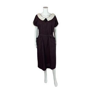 Puede incluir: Un vestido midi burdeos con cuello blanco Peter Pan y mangas cortas. El vestido tiene un cinturón y dos bolsillos.