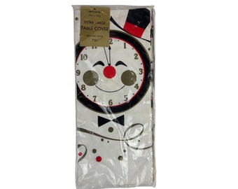 May include: White plastic-wrapped extra large table cover with a clock face design. The clock face has a smiling face with a red nose and a black bow tie. The clock face is surrounded by gold confetti and a black and white swirl design. The text "EXTRA LARGE TABLE COVER" and "79¢" are printed on the packaging.