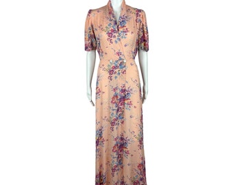 May include: A long, peach-colored dress with a floral print. The dress has a collared neckline, a double-breasted closure, and short sleeves.