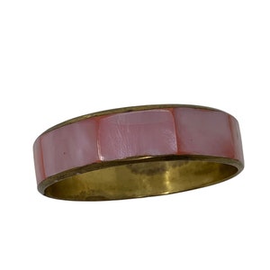 Puede incluir: Un brazalete de color rosa y dorado con un diseño geométrico. El brazalete está hecho de metal y tiene un acabado liso.