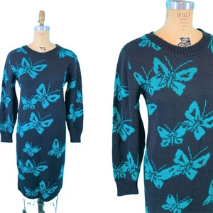 May include: A navy blue sweater dress featuring a repeating pattern of turquoise butterflies. The long-sleeved dress is displayed on a mannequin. The dress has a crew neck and a knee-length hemline.