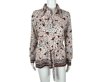 May include: A white long-sleeved shirt with a black, orange, and white polka dot pattern. The shirt has a collar, button closure, and a black belt.