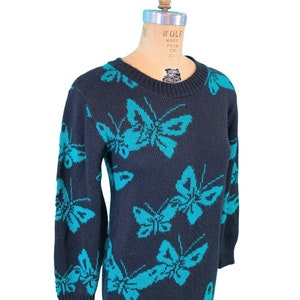 May include: A navy blue knit dress featuring a repeating pattern of turquoise butterflies. The long-sleeved dress has a crew neck and a knee-length hemline. The dress is displayed on a vintage dress form.