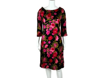 May include: A black dress with a floral print featuring pink and green flowers. The dress has a boat neck and three-quarter sleeves.