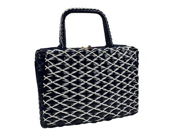 May include: A navy blue handbag with a white woven lattice design. The bag has a rectangular shape with a structured handle and a gold-colored clasp. The bag is made of a glossy material.