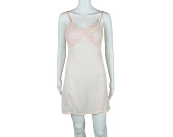 May include: A pale pink slip dress with delicate floral lace detailing on the bodice. The dress has thin straps and a straight skirt.