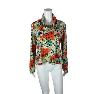 May include: A long-sleeved blouse with a cowl neck and a floral print. The print features red, blue, and yellow flowers on a cream background.