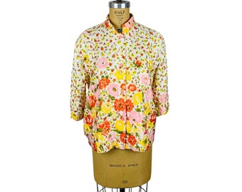 May include: A white button-up shirt with a floral print in shades of pink, yellow, and orange. The shirt has a mandarin collar and three-quarter sleeves.