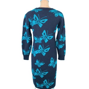 May include: A navy blue knit dress featuring a repeating pattern of turquoise butterflies. The long-sleeved dress is displayed on a mannequin, showcasing its form-fitting silhouette. The butterfly design adds a whimsical touch to the garment.
