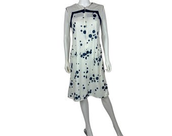Puede incluir: Vestido blanco vintage con estampado de lunares azul marino. El vestido sin mangas presenta cierre de cremallera, dos bolsillos delanteros y ribete azul marino. El vestido se exhibe en un maniquí.