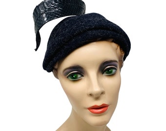 May include: A black felt hat with a black leather band. The hat is worn on a mannequin head with a neutral expression.