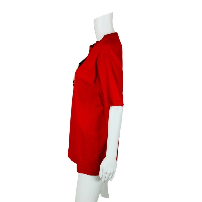 May include: A red short-sleeved t-shirt on a white mannequin. The t-shirt has a black design on the front.