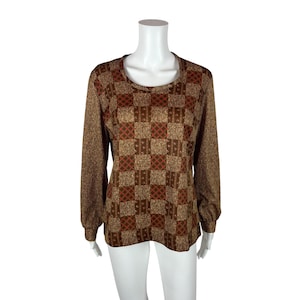 Puede incluir: Una blusa de manga larga marrón y dorada con un patrón a cuadros. La blusa tiene un escote redondo y un corte holgado.