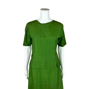 May include: A green two-piece skirt suit with a short-sleeved top and a knee-length skirt.