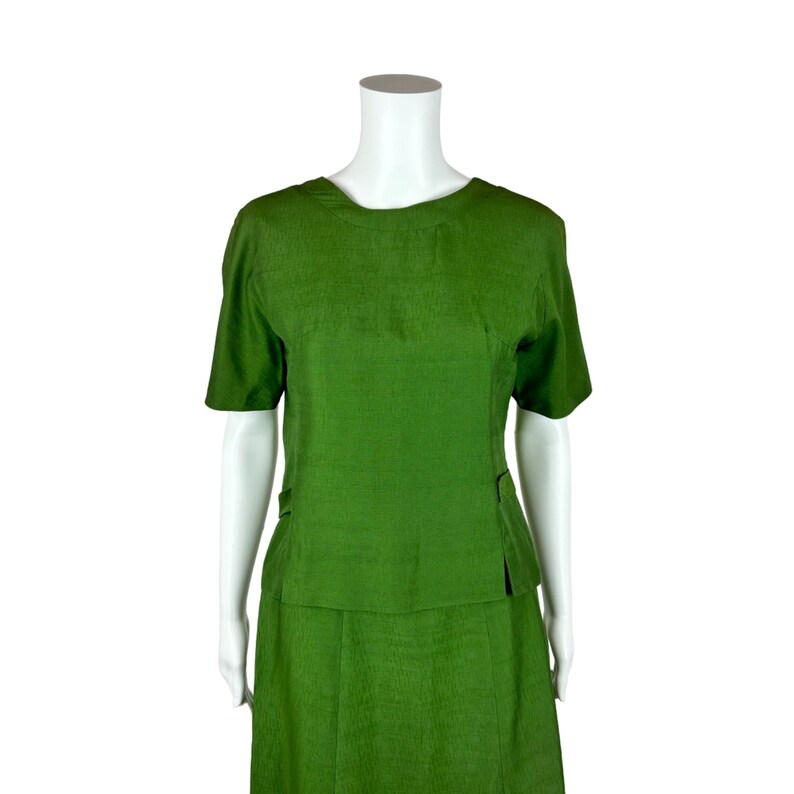 May include: A green two-piece skirt suit with a short-sleeved top and a knee-length skirt.