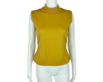 Pode incluir: Um suéter amarelo mostarda sem mangas com gola alta e uma fileira de pequenas decorações prateadas ao redor da gola.