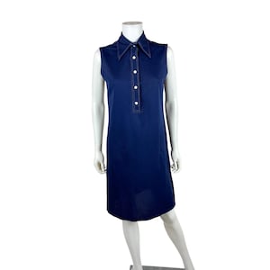 May include: A sleeveless navy blue dress with a collared neckline and a button-down placket. The dress features white stitching and a knee-length hemline. The dress is displayed on a mannequin.